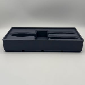 Op de afbeelding: Een donkergrijze rechthoekige opbergbak met gegoten compartimenten voor gereedschap. De bak heeft een laag profiel en is ontworpen om items veilig te bewaren. De compartimenten zijn gevormd om specifieke gereedschappen te passen.