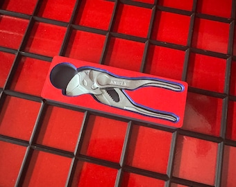 May include: A pair of silver and blue Knipex pliers, resting in a red and black box. The pliers are designed for gripping and cutting. The box is set against a red, grid-like background.
