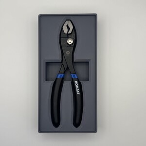 Op de afbeelding: Zwarte waterpomptang met blauwe handgrepen, gepresenteerd in een grijze tray. De tang heeft een zilveren draaipunt en het woord "KOBALT" is op de handgreep gedrukt. Deze tangen zijn ontworpen voor het grijpen en manipuleren van objecten.