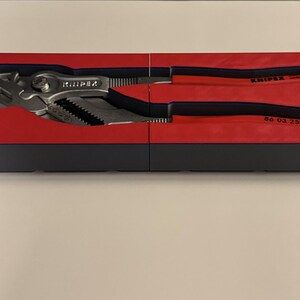 Op de afbeelding: Een set Knipex tangen in een rode en zwarte koffer. De tangen zijn zilverkleurig met zwarte en rode handgrepen. De koffer is rechthoekig en verdeeld in twee secties. De tangen zijn ontworpen om te grijpen en te draaien.