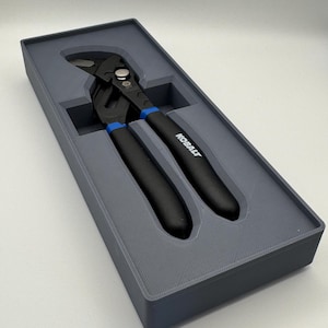 Peut inclure: Une pince multiprise KOBALT noire et bleue dans un étui en plastique gris. La pince a des poignées noires avec des accents bleus et le nom de la marque KOBALT imprimé sur le côté. L'étui est rectangulaire avec un intérieur moulé.