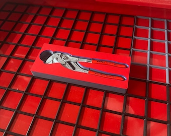 May include: A pair of pliers with red handles and silver jaws, resting in a blue and red box. The pliers are labeled with the brand name "KNIPEX". The tools are set inside a red toolbox with a black grid.