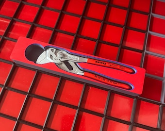 May include: A Knipex pliers wrench with red handles and silver jaws, resting in a red tray. The pliers are labeled with the brand name and model number. The tray is set within a red and black grid.