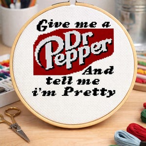 May include: Cross-stitch hoop art featuring the Dr. Pepper logo in red and white, and the phrase "Give me a Dr Pepper And tell me I'm Pretty" in black. The embroidery is set in a wooden hoop.