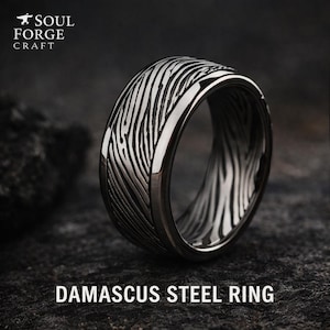 Pode incluir: Um anel de aço Damasco prateado com um padrão único. O anel apresenta um design escuro e texturizado. O texto "DAMASCUS STEEL RING" é exibido na parte inferior. O logotipo Soul Forge Craft está no canto superior esquerdo.