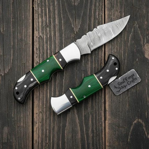A hand-forged Damascus folding knife with a gorgeous green wood handle — the swirling Damascus pattern is genuinely striking and screams 'a real craftsperson made this'.