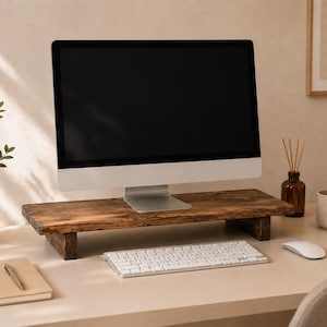 May include: A computer monitor with a black screen sits on a wooden monitor stand. A white keyboard and mouse are in front of the monitor. A small potted plant and a notebook are on the desk.
