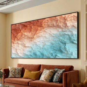 Puede incluir: Gran obra de arte enmarcada con un diseño de paisaje abstracto. La obra de arte muestra un diseño texturizado y en capas con colores que van del óxido y el naranja en la parte superior, pasando por el blanco, al turquesa en la parte inferior. El marco es negro.