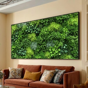 Könnte beinhalten: Ein großes, rechteckiges, gerahmtes Kunstwerk mit einer lebendigen grünen Wand aus verschiedenen Pflanzen. Das Kunstwerk hängt über einem braunen Sofa mit dekorativen Kissen. Die Pflanzen zeigen eine Reihe von Grüntönen und Texturen und schaffen eine natürliche, beruhigende Ästhetik.