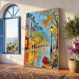 May include: A framed oil painting depicts a European street scene with a wet, reflective road. Buildings with lit windows line the street, and a bench with red roses sits in the foreground. The painting has a gold frame and is displayed near a window.