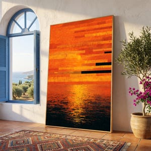 Op de afbeelding: Een groot ingelijst kunstwerk dat een zonsondergang boven water afbeeldt. Het kunstwerk heeft horizontale banden van oranje en zwart, met een gouden lijst. De scène wordt weerspiegeld in het water eronder. Het kunstwerk leunt tegen een witte muur naast een raam en een potplant.