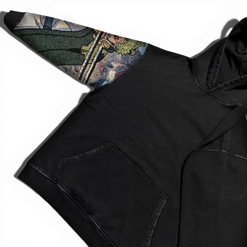 May include: Black hoodie with a front pocket and a hood. The left sleeve features a colorful, detailed tapestry design with green, blue, and gold tones. The hoodie is made of a soft, comfortable material.