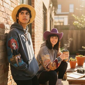 May include: Two people wearing gray hoodies with colorful anime character designs on the sleeves. One person wears a straw hat, the other a purple cowboy hat. They are sitting outside near a brick wall.