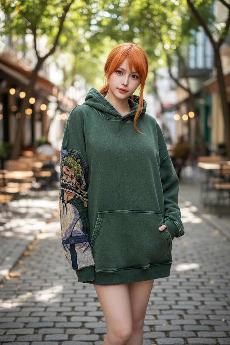May include: A dark green hoodie with a front pocket and a hood. The left sleeve features a colorful tapestry design. The hoodie is worn in an outdoor setting with trees and a brick-paved walkway.