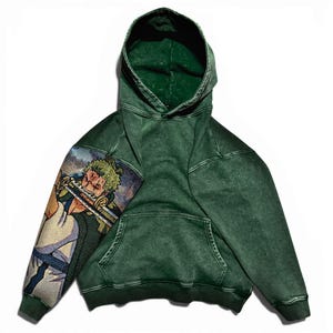 May include: Green hooded sweatshirt with a front pocket and a drawstring hood. The left sleeve features a colorful graphic of an anime character. The sweatshirt is made of a textured fabric.