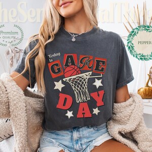 May include: Dark gray t-shirt with the words "Today is Game Day" in red and black, featuring a basketball and net design. The shirt has a vintage, distressed look and is paired with denim shorts.