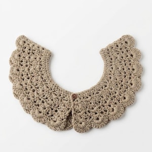 Op de afbeelding: Een beige gehaakte kraag met een geschulpte rand en een knoopsluiting. De kraag heeft een openwerk ontwerp. Dit handgemaakte accessoire is geschikt voor diverse outfits. De kraag is gemaakt van zacht garen.