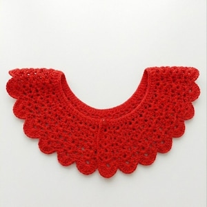 May include: A bright red, crocheted collar with a scalloped edge. The collar is made of a textured yarn and has a button closure at the front. The collar is a handmade accessory.