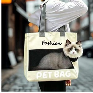 May include: A cream-colored canvas tote bag with grey shoulder straps, featuring a black mesh window and the text "Fashion" and "PET BAG" printed on the front. A fluffy, long-haired cat with white and brown fur is visible inside the mesh carrier.