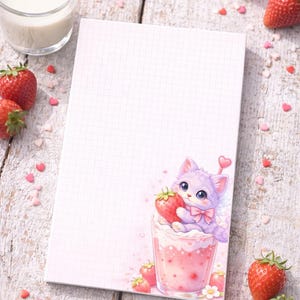 Puede incluir: Bloc de notas con un patrón de cuadrícula y una ilustración caprichosa de un gato morado sosteniendo una fresa en una bebida rosa. Fresas frescas y confeti en forma de corazón rodean el bloc de notas sobre una superficie de madera. Un vaso de leche está en el fondo.
