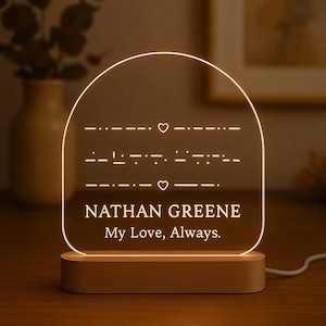 May include: A lit acrylic plaque with a wooden base. The plaque has a rounded top and displays Morse code, hearts, the name "NATHAN GREENE," and the phrase "My Love, Always." The light emits a warm glow.