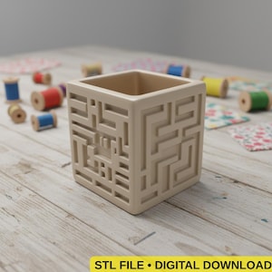 Puede incluir: Un recipiente cuadrado beige con un diseño de laberinto en los lados. Está sobre una superficie de madera clara, rodeado de carretes de hilo de varios colores. El texto "STL FILE • DIGITAL DOWNLOAD" está en la parte inferior.
