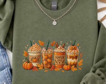 May include: A military green crewneck sweatshirt featuring a graphic of four iced coffee drinks topped with whipped cream and pumpkin accents. The center cup is labeled PUMPKIN SPICE. The design includes orange and yellow autumn leaves.