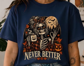 May include: A navy blue t-shirt featuring a graphic of a skeleton wearing sunglasses and a plaid headband, holding a jack-o'-lantern mug. The design includes autumn leaves, a pumpkin, and the text NEVER BETTER in a bold, light-colored font.