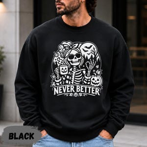 May include: A black crewneck sweatshirt featuring a white graphic print of a skeleton wearing sunglasses and a hair bow, holding a jack-o'-lantern mug. The design includes bats, trees, and the text NEVER BETTER in a bold, stylized font.