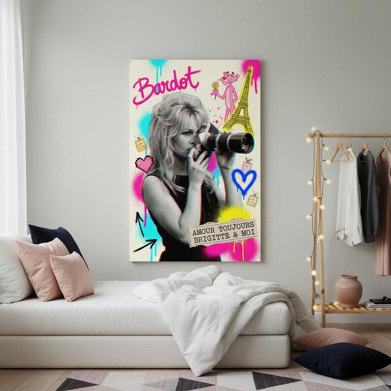 Może przedstawiać: Wydruk na pł&oacute;tnie przedstawiający czarno-biały obraz Brigitte Bardot trzymającej aparat fotograficzny, z kolorowymi akcentami w stylu graffiti. Grafika zawiera r&oacute;żowe słowo "Bardot", r&oacute;żową panterę i wieżę Eiffla.