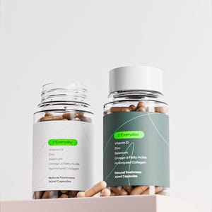 Puede incluir: Dos frascos de suplementos de vidrio transparente con tapas blancas. Las etiquetas dicen "2 Everyday" y enumeran ingredientes como vitamina D, zinc y ácidos grasos omega-3. Los frascos contienen cápsulas marrones. También se ve el texto "Natural freshness 30ml Capsules".