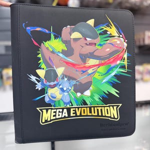 May include: Black card binder featuring a colorful graphic of two cartoon creatures with the text "MEGA EVOLUTION". The binder has a stitched border and is designed for trading cards.