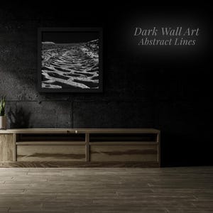 Peut inclure: Une impression encadrée en noir et blanc d'un paysage texturé est suspendue au-dessus d'un meuble TV en bois. L'art mural est intitulé "Dark Wall Art Abstract Lines". Une plante en pot est posée sur la console, et le sol est en bois.