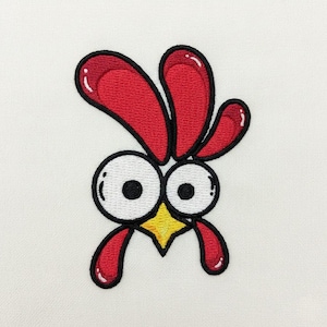 Puede incluir: Parche bordado con la cabeza de un gallo de dibujos animados. El gallo tiene ojos grandes y anchos, un pico amarillo y cresta y barbilla rojas. El diseño está delineado en negro sobre un fondo blanco.