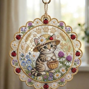 May include: Embroidered round wall hanging featuring a tabby kitten wearing a straw hat with a daisy and strawberry. The kitten holds a basket amidst flowers and ladybugs. The design includes wheat stalks and paw prints.