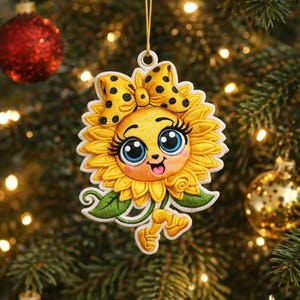 May include: Embroidered sunflower Christmas ornament with a smiling face, blue eyes, and a yellow bow with black polka dots. The ornament is hanging on a Christmas tree with red and gold ornaments.
