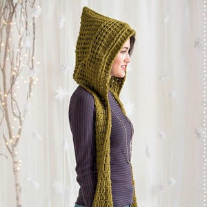 Könnte beinhalten: Ein grüner gehäkelter Kapuzen-Schal. Die Kapuze ist spitz und der Schal hängt nach vorne. Das Kleidungsstück ist aus einem strukturierten, offen gewebten Garn gefertigt. Die Person trägt ein gestreiftes Oberteil.