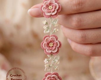 Puede incluir: Primer plano de un diseño floral de ganchillo. El diseño presenta tres flores rosas y crema con centros amarillos, conectadas por un tallo con pequeñas hojas verdes. El texto "Crochet Pattern" está en un marco circular.