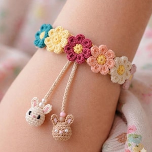May include: A handmade crochet bracelet featuring colorful flower accents in shades of blue, yellow, pink, and white. Two dangling bunny charms with pearl accents add a whimsical touch to this unique accessory.