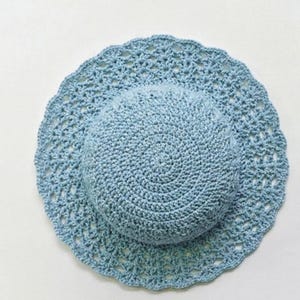 Peut inclure: Un chapeau de soleil en crochet bleu clair avec un large bord festonné. La couronne du chapeau est de conception circulaire pleine, tandis que le bord présente un motif ajouré. Le chapeau est fait à la main et semble être en fil de coton.