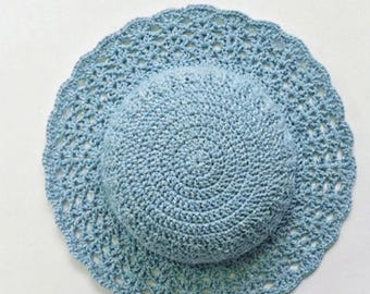 Puede incluir: Un sombrero de sol de ganchillo azul claro con un ala ancha y festoneada. La copa del sombrero tiene un diseño circular sólido, mientras que el ala presenta un patrón calado. El sombrero está hecho a mano y parece estar hecho de hilo de algodón.