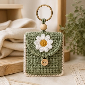 Può includere: Una pochette all'uncinetto color verde salvia con un'applicazione a forma di margherita bianca con centro giallo sulla patta. La pochette presenta un bordo beige chiaro, una chiusura con bottone in legno, una perlina in legno e un portachiavi dorato.