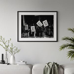A black and white photograph of a group of people holding up signs with the numbers "10" and "10" on them, suggesting a competition or event.