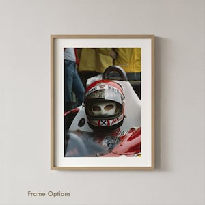 May include: Framed print of a vintage racing car driver wearing a red and white helmet with the Marlboro logo. The driver has a white face covering. The car is red and white. The image is in a light wood frame.