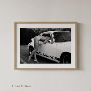 A black and white photograph of a person leaning on a car, with the car's design visible on the side.
