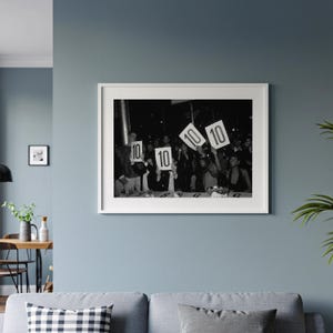 The image is a framed black and white photograph of a group of people holding up signs with the numbers "10" and "10" on them.