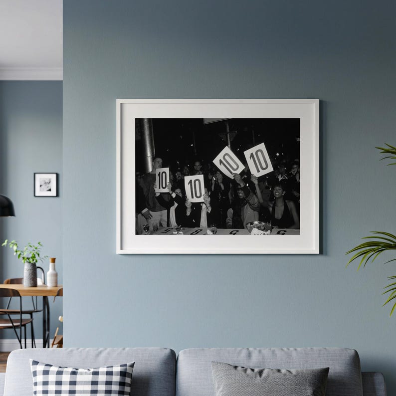 The image is a framed black and white photograph of a group of people holding up signs with the numbers "10" and "10" on them.
