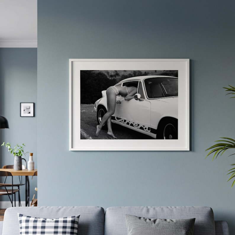 A framed black and white photograph of a person leaning out of a car window, with a couch and other decor visible in the background.