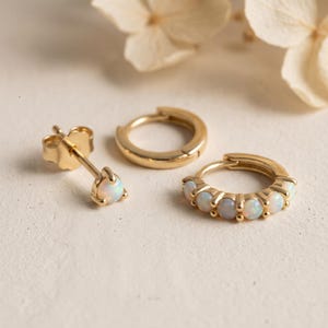 May include: A set of gold jewelry consisting of one single stud earring with a round opal, one plain gold hoop earring, and one gold hoop earring featuring a row of five small round opals set along the front edge of the hoop.