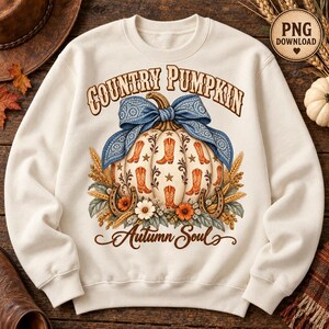 May include: A cream-coloured crewneck sweatshirt featuring a graphic of a pumpkin decorated with cowboy boot illustrations, stars, and a blue bandana-print bow. The text reads "COUNTRY PUMPKIN" above and "Autumn Soul" below, surrounded by wheat and flowers.